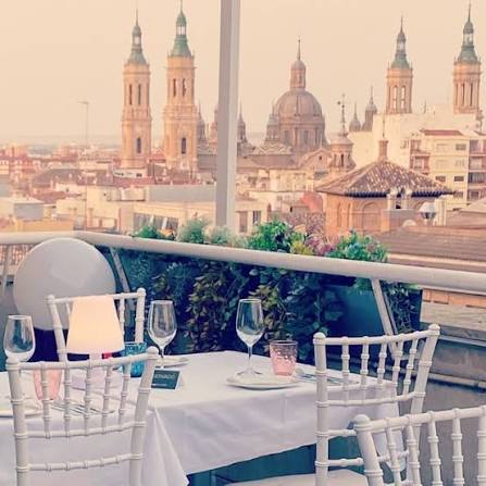 Terraza del Apartahotel Los Girasoles con una mesa preparada y, al fondo, las torres y cúpulas de la Basílica del Pilar
